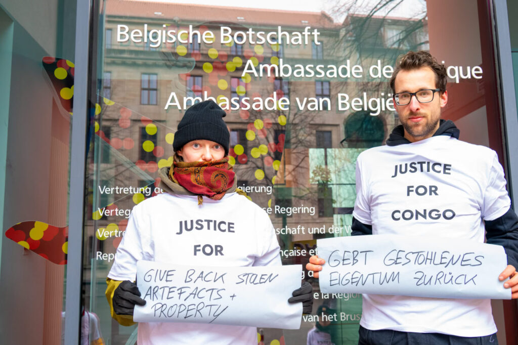 Zwei Personen halten Poster vor der belgischen Botschaft.