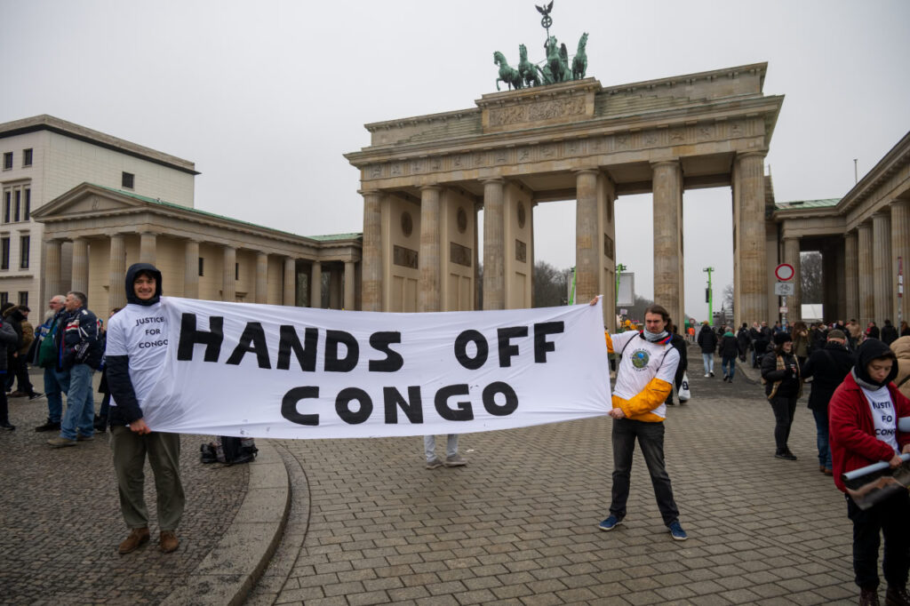 Ein Banner vor dem Brandenburger Tor, gehalten von zwei Menschen, mit der Aufschrift "Hands off Congo".